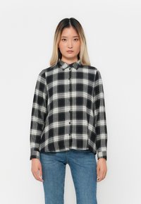 Svart og hvitt rutete skjorte med krage, lange ermer og avslappet passform, kombinert med blå jeans.