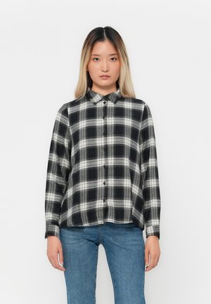 Svart og hvitt rutete skjorte med krage, lange ermer og avslappet passform, kombinert med blå jeans.