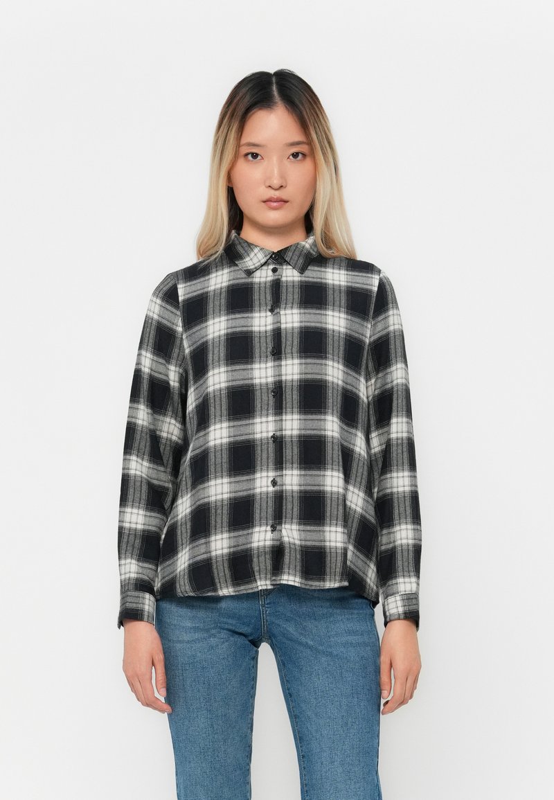 Svart og hvitt rutete skjorte med krage, lange ermer og avslappet passform, kombinert med blå jeans.