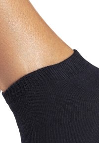 Schwarze gerippte Knöchelsocke aus strukturiertem Stoff mit einem engen Elastikbund, der Haut von der Knöchel- bis zur Mittelfußregion sichtbar macht.