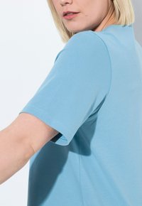 Svetle modré tričko s krátkým rukávem vyrobené z měkké tkaniny; má kulatý výstřih a rovný střih, s minimálními viditelnými švy.