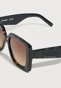 Négyzet alakú napszemüveg teknőspáncél mintájú elülső résszel és fekete szárakkal. Barna átmenetes lencsék és geometrikus díszítések a kereten. "KARL LAGERFELD" márkajelzéssel.