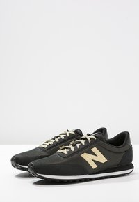 Czarne sneakersy wykonane z tkaniny i materiałów syntetycznych, z teksturowanym cholewką, złotymi akcentami i białą podeszwą.