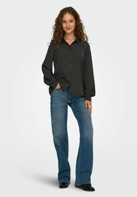 Mörkgrå knäppblus med långa ärmar, i kombination med ljusblå urtvättade utsvängda jeans. Slätt tyg, avslappnad passform och subtil lyster.
