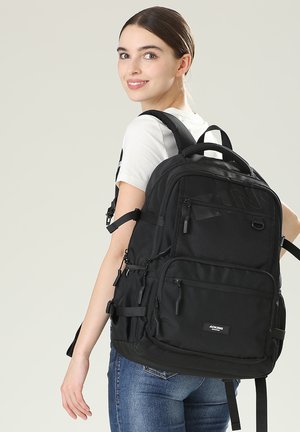 Sac à dos noir en tissu durable, comportant plusieurs poches zippées, des bretelles réglables et une poignée supérieure pour un transport facile.