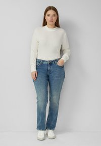 Biały prążkowany top z długim rękawem zestawiony z niebieskimi jeansami o prostych nogawkach i białymi trampkami. Prosty design, standardowy krój, klasyczna faktura denimu.