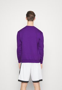 Sweat-shirt violet à manches longues et col rond, en tissu texturé. Associé à un short blanc avec des accents noirs.