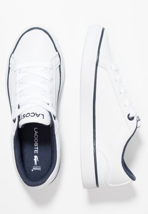 Zapatillas blancas Lacoste con forro azul marino, borde negro en las suelas, cordones atados, vistas desde arriba y de lado sobre un fondo blanco.