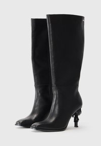 Black leather knee-high boots with a pointed toe, tapered design, and unique accessory detailing on the black heel. Smooth texture.