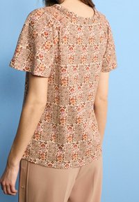 Blusa de manga corta con un patrón floral en tonos pastel, que presenta un escote texturizado, ajustada en los hombros, con un corte relajado y una tela suave.