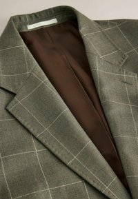Blazer vert à carreaux blancs en motif quadrillage avec une doublure intérieure marron, présenté plié avec les détails du col et du revers visibles.