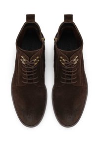 Brown suede ankle boots with a smooth texture, featuring six eyelets for laces, brass hardware accents, and a rounded toe design.