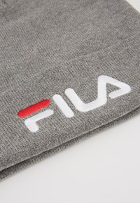 Gorro de punto gris con una textura suave, que presenta un destacado logo bordado en blanco de "FILA" y un pequeño acento rojo dentro del diseño del logo.