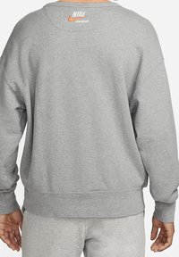Grijze sweatshirt met een losse pasvorm, geribbelde manchetten en onderrand, met een oranje Nike-logo op de achterkant nabij de halslijn. Zachte textuur.