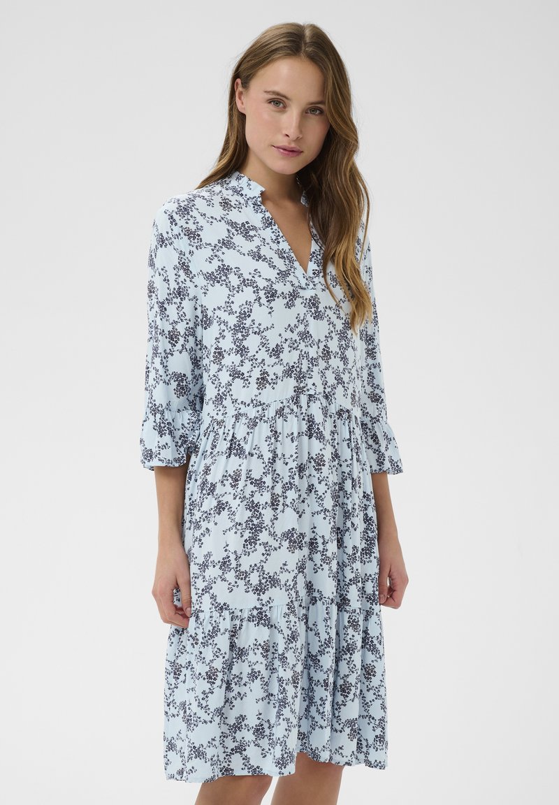 Robe bleu clair à motif floral avec des accents bleu marine, dotée d'un col en V, de manches trois-quarts et d'une jupe à volants.