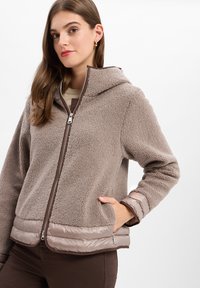 Brown fleece jacket with a plush texture, zip closure, and a hood. Features padded brown accents at the hem and cuffs. Two side pockets.