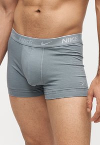 Gros plan d'une personne portant un boxer gris Nike avec une large ceinture et un petit logo Nike sur la cuisse gauche.
