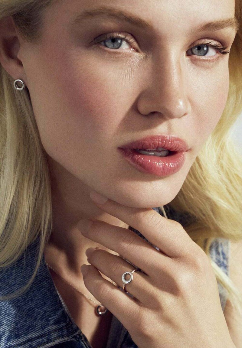 Silver cirkulära stiftörhängen, en delikat ring med en cirkulär detalj och ett enkelt halsband som bärs mot ljus hy och blont hår.