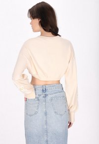 Pulover bej scurt, cu mâneci lungi, având broderie florală pe mâneci. Asortat cu o fustă din denim deschis la culoare, cu talie înaltă.