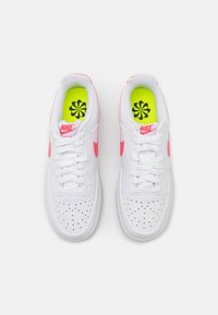 Valged Nike tossud roosa aktsentidega, perforeritud ülemine osa ja valged nööbid. Heledat roheline sisetallad sisaldavad musta lillemustrit.