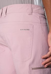 Pink shorts made of lightweight fabric, featuring a back pocket with an angled design and embossed "OAKLEY" logo on the waistband.