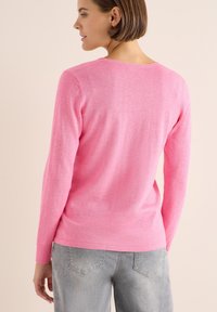 Langdurige roze trui van zachte stof, met een ronde halslijn, geribde manchetten en een zachte textuur. Draag met grijze broek.