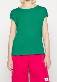 Zelené tričko s krátkým rukávem vyrobené z měkké látky, kulatý výstřih, kombinované s růžovými cargo šortkami s kapsami a nášivkou s logem.