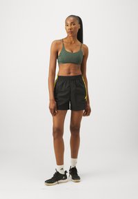 Sportisks apģērbs, kas sastāv no zaļas teksturētas šortiem un melniem šortiem ar dzeltenām sānu svītrām. Kopā ar melniem apaviem un baltām sporta zeķēm.