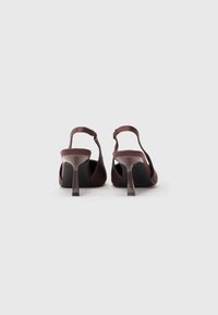 Sapatos de salto slingback castanhos com um acabamento suave, apresentando um salto esguio e uma tira ajustável. Solas interiores pretas e um design de bico redondo.