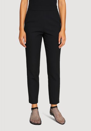 Pantaloni neri a gamba affusolata con una texture liscia e cintura elastica, abbinati a stivaletti neri in rete con accenti metallici.