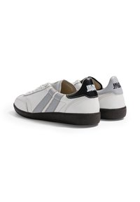 Paire de baskets en cuir blanc avec des rayures grises, des languettes de talon noires comportant un texte blanc "JAVA", et des semelles en caoutchouc noir texturé.