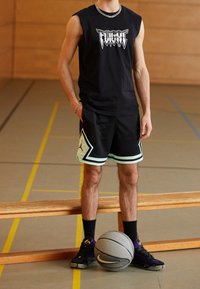 Černé bezrukávové tričko s grafikou "FLIGHT", černé šortky s akvamarínovými akcenty a logem, černé tenisky, stojící na tělocvičném podlaze s basketbalem.