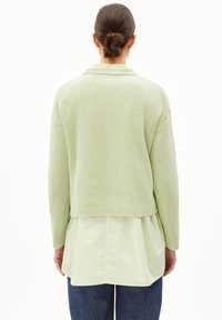 Vaaleanvihreä neulepaita, jossa on ribbikuvio, lyhennetty malli ja V-pääntie, yhdistettynä vaaleamman vihreään kerroshirtseen sen alla.