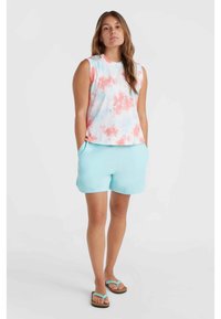 Ärmelloses Batik-Oberteil in Pastellpink, Blau und Weiß; kombiniert mit hellblauen Shorts. Das Modell trägt schwarze Flip-Flops mit türkisfarbenen Riemen.