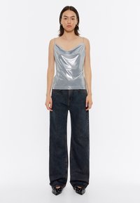 Top sin mangas de cuello en cowl plateado con tirantes finos, que presenta una textura brillante y reflectante, combinado con unos pantalones de mezclilla oscuros de pierna ancha de cintura alta.