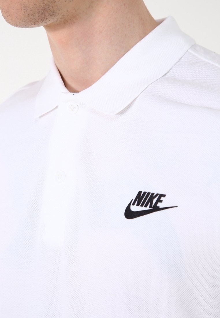 Bílá polokošile s texturovanou tkaninou, s černým logem Nike na levé hrudi a dvouknoflíkovým zapínáním u límce.