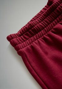 Burgundské joggery s textúrovaným elastickým pásom. Tkanina je mäkká, s hladkým povrchom a voľným strihom.