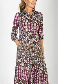 Sukienka z długim rękawem zapinana na guziki, z kolorowym geometrycznym wzorem w odcieniach różu, brązu, turkusowego i białego. Zawiera kieszenie.