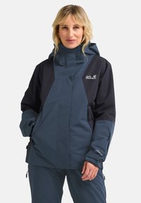 Wasserdichte Jacke in Dunkelblau und Schwarz, ausgestattet mit einem hohen Kragen, verstellbaren Manschetten und Reißverschlusstaschen. Strukturierter Stoff mit sichtbarem Branding.