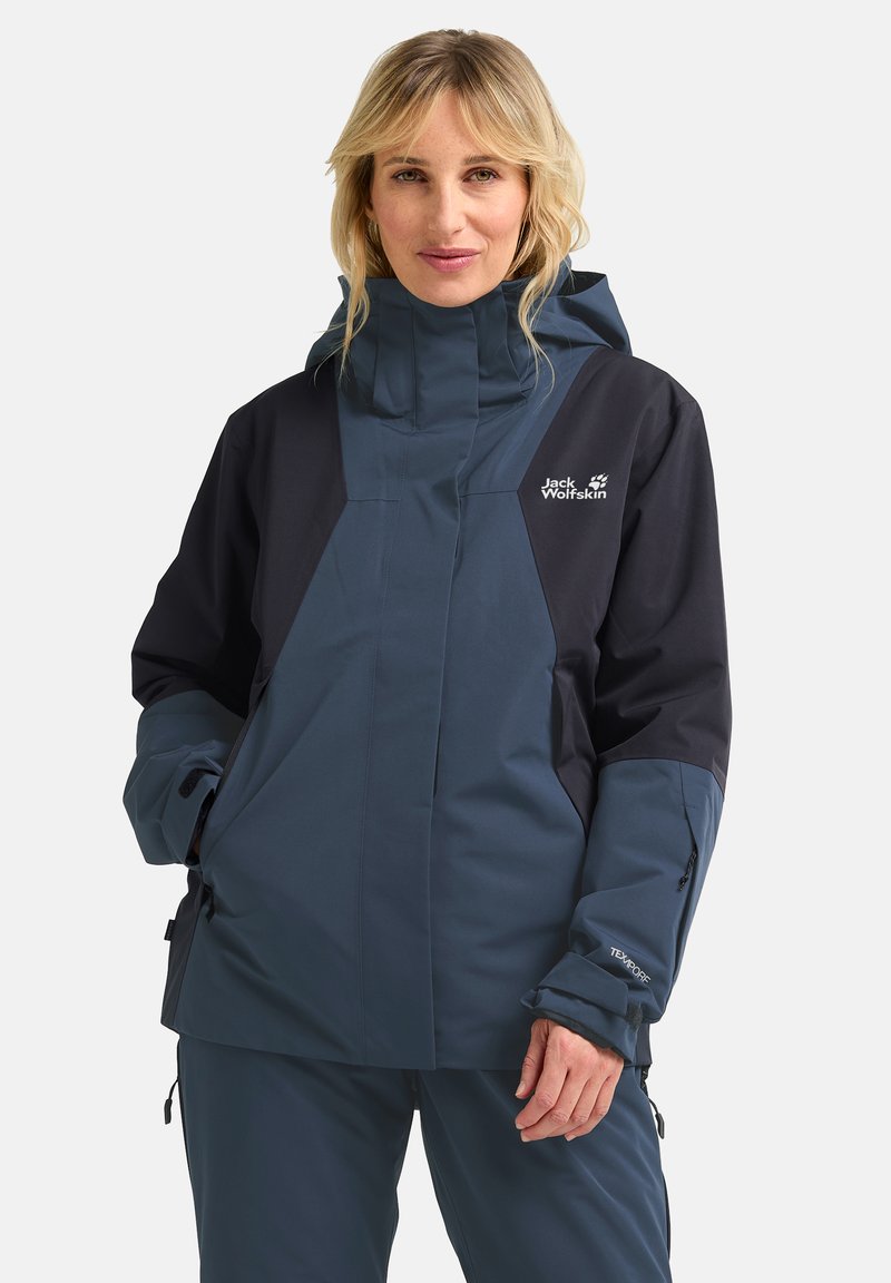 Wasserdichte Jacke in Dunkelblau und Schwarz, ausgestattet mit einem hohen Kragen, verstellbaren Manschetten und Reißverschlusstaschen. Strukturierter Stoff mit sichtbarem Branding.