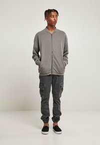 Grå zippad sweatshirt med krage, bärs över mörka cargo-byxor. Byxorna i jogger-stil har flera fickor och elastiska muddar. Svarta slip-on skor.