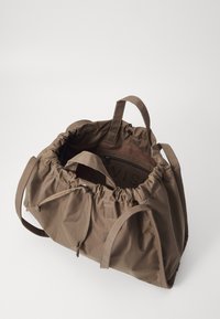 Bruine stoffen tas met een gathered bovenkant, twee korte handvatten en een ritsvak aan de binnenkant. Gladde textuur met zichtbare stiksels.