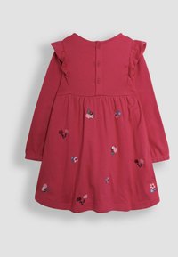 Langärmliges pinkes Kleid mit Rüschenschulterakzenten, das mit gestickten Blumenmustern versehen ist. Knopfverschluss hinten mit rundem Ausschnitt.