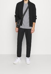 Musta ribatty zip-up neuletakki, harmaa t-paita, mustat housut ja valkoiset sneakersit mustilla yksityiskohdilla. Pieni musta olkalaukku. Yksinkertainen muotoilu.