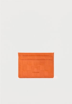Tarjetero naranja con patrón de cuadros en relieve y tres ranuras para tarjetas, con costuras sutiles y el nombre de la marca "J.LINDEBERG" en el frente.