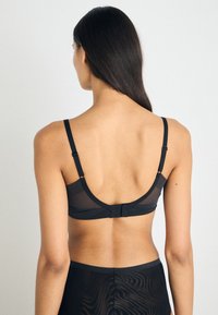 Soutien-gorge noir en tissu transparent, avec des bretelles réglables et une fermeture �à crochets au dos. Texture lisse avec un design de dos décolleté.