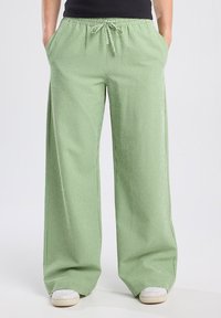 Pantalons larges à carreaux verts avec une taille élastique et un cordon de serrage, comprenant deux poches latérales et une texture de tissu léger.