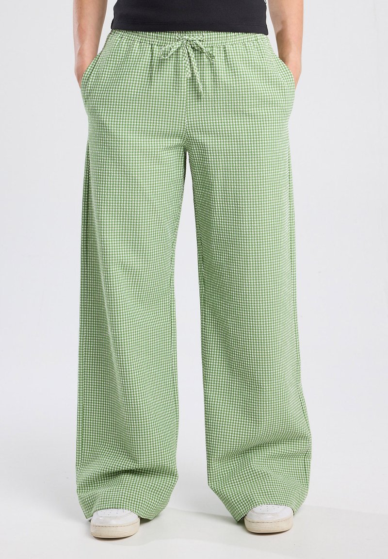 Pantalons larges à carreaux verts avec une taille élastique et un cordon de serrage, comprenant deux poches latérales et une texture de tissu léger.