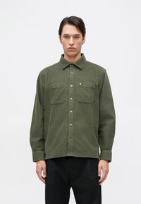 Camisa verde oliva de botones con mangas largas, dos bolsillos en el pecho y un pequeño logo amarillo en el bolsillo izquierdo. Tejido de mezcla de algodón.