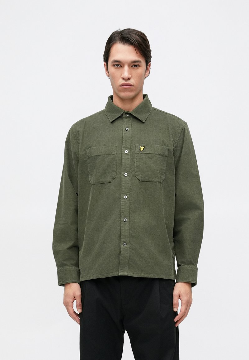 Camisa verde oliva de botones con mangas largas, dos bolsillos en el pecho y un pequeño logo amarillo en el bolsillo izquierdo. Tejido de mezcla de algodón.